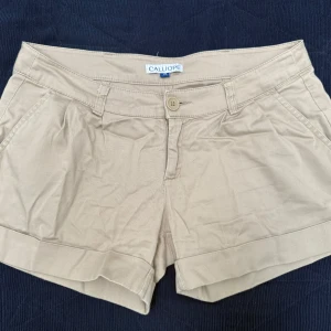 Beige shorts från Calliope - Snygga beige shorts från Calliope i storlek M. De har en klassisk design med knapp och dragkedja framtill. Perfekta för en avslappnad stil. Materialet är mycket skönt att ha på sig. 