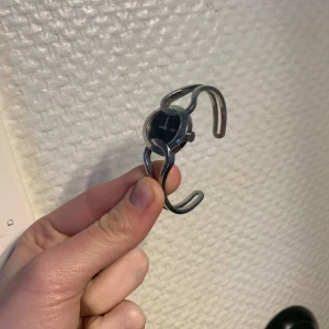 Elegant armbandsur i silver - Snygg och stilren klocka med en unik design. Den har en svart urtavla och ett öppet armband i silverfärg. Perfekt för dig som vill ha något annorlunda och elegant på handleden. Inte inställd rätt