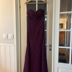 Vinröd långklänning från Mori Lee!! - Elegant vinröd långklänning från Mori Lee med spetsdetaljer och axelbandslös design. Perfekt för formella tillfällen med sin figurnära passform och vackra fall.