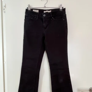 Svarta bootcut jeans från Levi's - Snygga svarta bootcut jeans från Levi's med klassisk femficksdesign och knappgylf. Perfekta för en stilren look med en touch av retro. Passar bra till både sneakers och klackar.