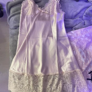 Ljusrosa sidenklänning med spetsdetaljer - Elegant ljusrosa sidenklänning med vackra spetsdetaljer vid byst och nederkant. Klänningen har smala axelband och en söt rosett framtill. 