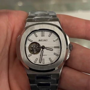 Silverfärgad klocka från Seiko - Säljer en stilren silverfärgad klocka från Seiko med automatisk urverk och ett öppet hjärta på urtavlan. Klockan har en borstad metallfinish och ett armband i rostfritt stål. Perfekt för den som gillar en klassisk och elegant stil.