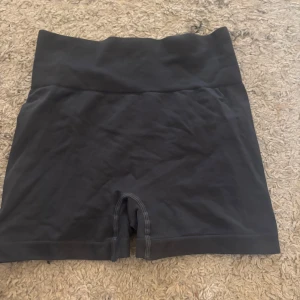 Mörk gråa shorts med hög midja - Säljer ett par mörkgrå shorts med hög midja, tillverkade av 92% polyamid och 8% elastan. Perfekta för träning med en bekväm och stretchig passform. De har en ribbad midja för extra komfort.