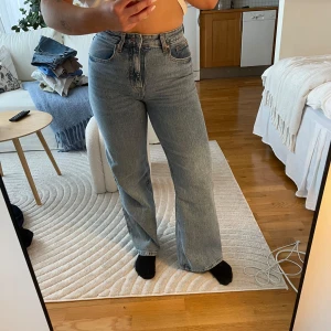 Blå jeans från H&M - Säljer ett par klassiska blå jeans från H&M. De har en hög midja och en rak passform som ger en avslappnad look. Perfekta för en casual stil. Jeansen har fem fickor och stängs med dragkedja och knapp. Litet skav på låret, se bild.
