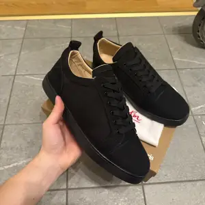 Snygga svarta sneakers med en iögonfallande röd sula. Skorna har snörning och är tillverkade i mocka. Perfekta för en stilren look.