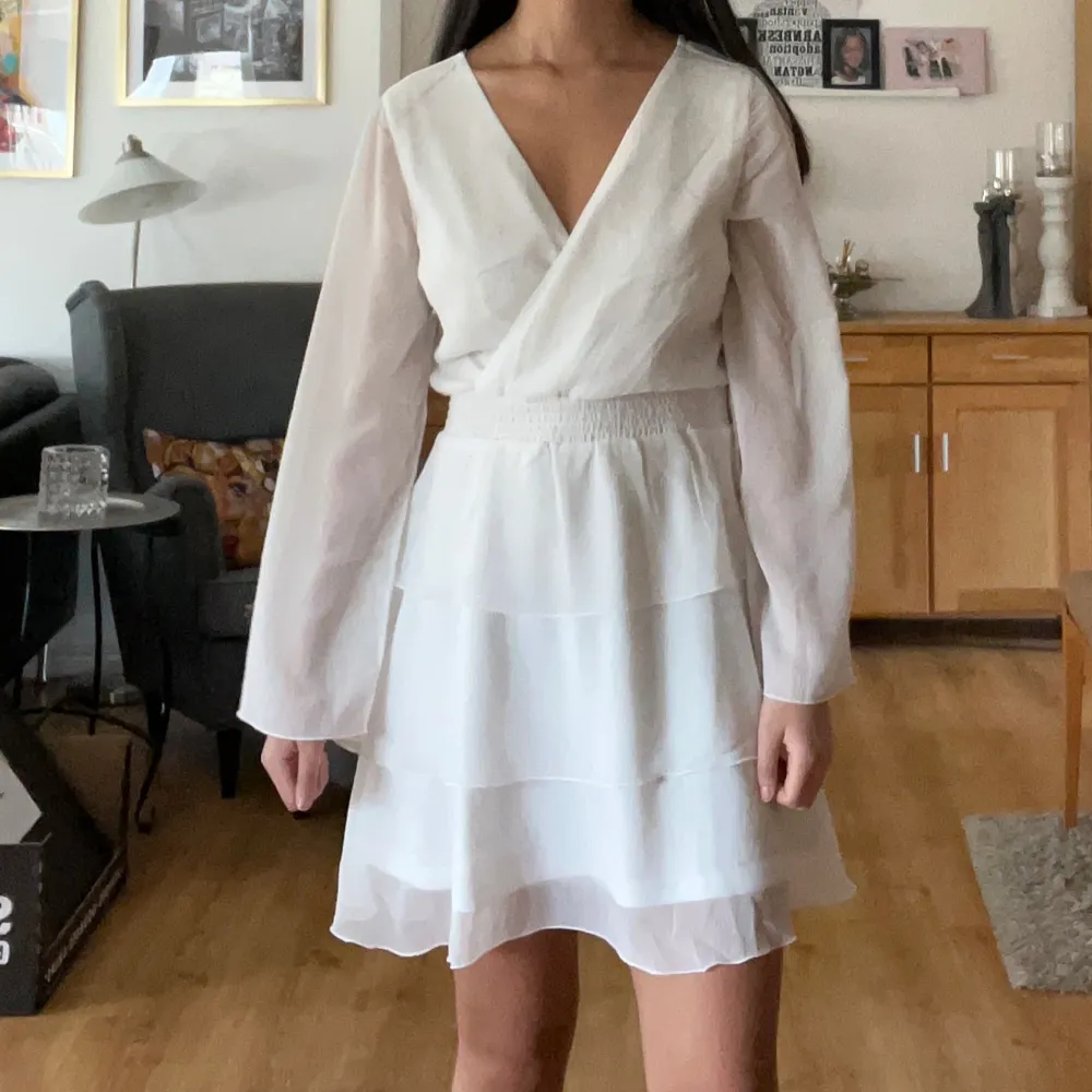 Säljer min studentklänning! Det är en söt vit omlottklänning med v-ringning och långa ärmar. Klänningen elastisk midja och volangdetaljer på kjolen. Perfekt för sommarens alla tillfällen!. Mekot.