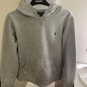 Ralph Lauren Hoodie grå - Säljer en grå hoodie från Polo Ralph Lauren. Den har en ficka framtill och en liten broderad logga på bröstet. Perfekt för en snygg stil. Köpt från kids brand store teen. Hör av dig vid intresse!          Barn-storleken L motsvarar ungefär S. 