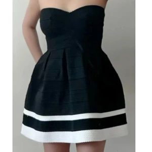 Svart axelbandslös klänning med vita ränder - Snygg svart axelbandslös klänning med vita ränder längst ner. Perfekt för en kväll ute eller en speciell tillställning. Klänningen har en elegant passform och en kort längd som ger en chic look.