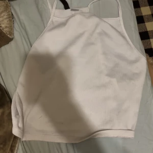 Vit linnetopp från H&M Divided - Säljer en stilren vit linnetopp från H&M Divided. Toppen har smala axelband och en enkel design som passar perfekt till sommaren. Perfekt för en avslappnad look!