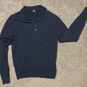 Mörkblå pikétröja från Uniqlo - Säljer en stilren mörkblå pikétröja från Uniqlo. Tröjan har en klassisk krage med två knappar och långa ärmar. Perfekt för en avslappnad men ändå snygg look.