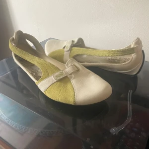 Beige och gröna puma-ballerinaskor  - Snygga ballerinaskor i beige och grönt med rund tå och en grön rem över foten.  Köpta second hand men endast använda en gång. Det finns vissa slitningar inuti skorna men inget som märks när de är på! 