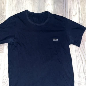 Mörkblå t-shirt från Hugo Boss - En stilren mörkblå t-shirt från Hugo Boss med diskret logga på bröstet. Klassisk rund halsringning och korta ärmar. Perfekt basic-plagg i garderoben, tillverkad i mjuk bomull för skön känsla hela dagen. Passar även Xs väldigt bra 