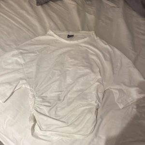 Vit topp med snörning från Gina Tricot - Säljer en vit topp från Gina Tricot i storlek S. T-shirten har korta ärmar, rund halsringning och en snygg snörningsdetalj på ena sidan som ger en cool twist. Perfekt att matcha med jeans eller kjol för en fräsch look.