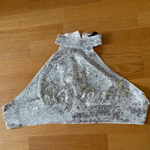 Glittrig guldig halterneck topp - Säljer en glittrig halterneck topp i guld  med paljetter över hela framsidan. Toppen har hög krage, knäppning i nacken och knytning i ryggen. Perfekt för dig som vill sticka ut och glänsa på festen!