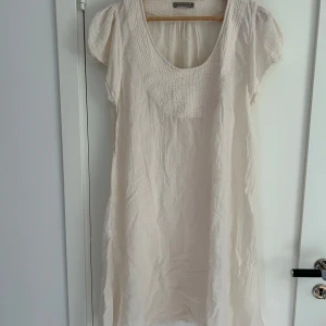 Ljusbeige linneklänning Rabens Saloner - Superfin ljusbeige kortklänning från Rabens Saloner i luftig linne. Den har korta ärmar, rund hals med snyggt strukturmönster och avslappnad passform. Perfekt för varma dagar och enkel att styla med accessoarer.