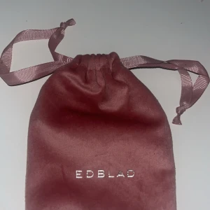 Rosa sammetsfodral från Edblad - Säljer ett lyxigt rosa sammetsfodral från Edblad med dragsko och matchande band. Perfekt för att förvara smycken som ringar, halsband, armband eller örhängen. Fodralet har en mjuk känsla och stilren design med Edblad-logga i silver.