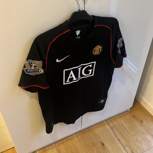 Manchester United Ronaldo 7 Nike tröja - Säljer en svart Manchester United fotbollströja från Nike med AIG som sponsor och Ronaldo 7 på ryggen. Tröjan har röda detaljer, korta ärmar och Premier League-patch på båda ärmarna. Perfekt för  fotboll eller samling. Inga defekter! Mvh  ItsForfits🌟
