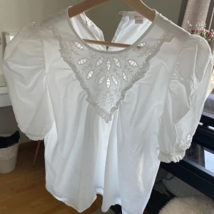 Vit blus med puffärm från Gina Tricot - Supersöt vit blus från Gina Tricot med puffiga korta ärmar och vackert broderad spetsdetalj framtill. 