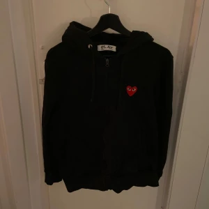 Svart zip hoodie från Comme des Garçons Play - Hej, jag säljer svart hoodie från Comme des Garçons med det ikoniska röda hjärta broderat på bröstet. Hoodien är väldigt bekväm och i toppskick då den inte har nå defekter eller fläckar. Pris kan diskuteras! 