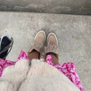Fransskor - Unika sneakers i beige mocka med coola fransdetaljer och snörning framtill. Skorna har en platt vit sula och grova stickade sömmar längs kanterna. Perfekta för dig som vill sticka ut med en boho-inspirerad stil.