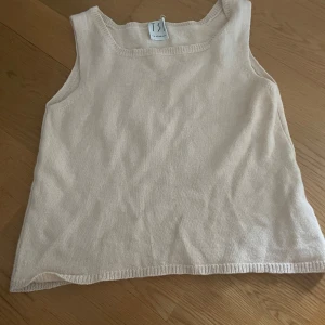 Beige kashmir linnetopp från TSE - Superskön och stilren beige linnetopp från TSE i lyxig kashmir. Toppen är ärmlös med rund halsringning och har en mjuk, stickad känsla. Perfekt för dig som gillar minimalistisk och clean stil.