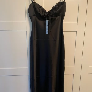 Svart satinklänning med spetsdetaljer - Supersnygg svart långklänning från Gina i satin med tunna axelband och spetskant vid bysten. Klänningen är enbart provad och i storlek 34! Nypris 499kr