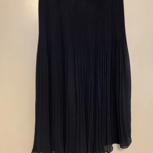 Marinblå plisserad kjol från H&M - Marinblå plisserad kjol från H&M i storlek 40. Kjolen har ett snyggt fall och är tillverkad i ett lätt, flowy material som ger en elegant siluett. Perfekt att styla med sneakers eller boots för en cool look.
