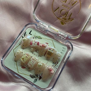 KawaiiChai(L);Short Almond - Supergulliga gelé press-on naglar i storlek L: 17 mm, 12,5 mm, 13 mm, 12 mm, 10 mm , med glittrig nude bas och 3D dekorationer som hjärtan, rosetter, bubble tea och kawaii-hello Kitty motiv. Naglarna har en glansig finish och detaljer i rosa, vitt och guld. Perfekt för dig som vill ha unika och lekfulla naglar.