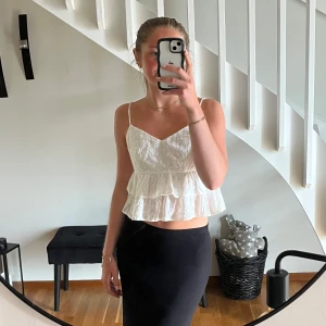 Vit volangtopp med broderi - Superfin vit linnetopp med tunna axelband, v-ringning och dubbla volanger. Toppen har broderade små blommor, är något croppad och helt oanvänd. Perfekt för varma dagar och ger en söt, somrig vibe.