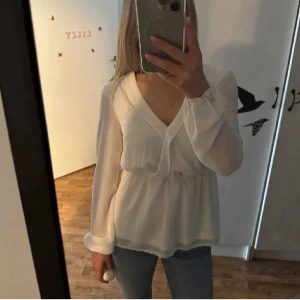 Vit omlottblus med v-ringning - Säljer en superfin vit blus med omlott och v-ringning. Blusen har långa, lite transparenta ärmar med resår vid handlederna och ett lätt rynkat midjeparti som ger en snygg siluett. Perfekt att styla med jeans eller kjol för en fräsch look.