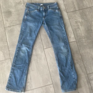 Replay jeans med gult märke - Snygga blå jeans från Replay med raka ben och klassisk femficksdesign. Baksidan har dekorativa sömmar på fickorna och ett unikt gult Replay-märke i skinn med blommönster. Jeansen har normal passform och är tillverkade i mjukt denimtyg. Storlek 150/26!