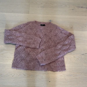 Stickad ljusrosa tröja från LMTD - Superfin stickad tröja från LMTD i en ljusrosa nyans. Tröjan har ett snyggt hålmönster i hela plagget och ribbade muddar vid ärmslut och nederkant. Perfekt för dig som gillar en mysig och trendig look.