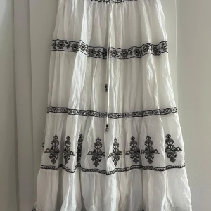 Vit långkjol med broderi från Zara - Superfin vit långkjol från Zara med svarta broderade detaljer och snörning i midjan. Passar även mig som har storlek S avsikten med storleken är att kjolen ska bli lång💗💗
