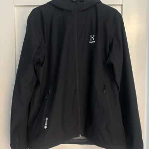 Haglöfs Chaos GTX Jacket Men - Svart vindjacka från Haglöfs i Gore-Tex-material med huva och hel dragkedja framtill. Jackan är sparsamt använd och är storlek M.