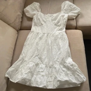 Vit kort klänning från Parisian - Supersöt vit kort klänning från Parisian med puffärmar och volangkant nertill. Klänningen har en feminin passform med markerad midja och dragkedja i sidan. Perfekt för sommarens alla tillfällen!