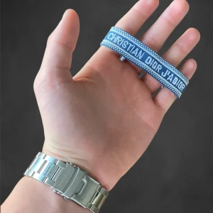 Blått armband från Christian Dior - Snyggt blått armband från Christian Dior med texten 'Christian Dior J'Adior' broderad i vitt. Armbandet har en vävd struktur och justerbar knytning för perfekt passform. Perfekt accessoar för att lyfta din outfit.