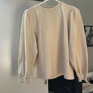 Beige sweatshirt med puffärmar - En stilren beige sweatshirt med puffiga långärmar och rund halsringning. Tröjan har ribbade muddar vid ärmslut och hals, vilket ger en snygg och bekväm passform. Perfekt för dig som gillar en enkel men trendig look.