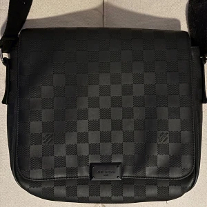 Svart väska  - Snygg svart axelväska med klassiskt-rutmönster. Väskan har justerbar axelrem, lock och flera fack inuti. Tillverkad i skinn och textil, perfekt för dig som gillar stilrena och lyxiga accessoarer.