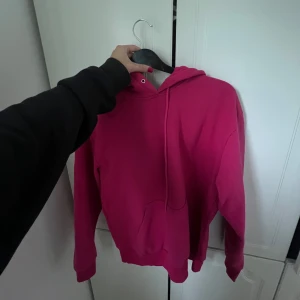 Mörkrosa hoodie med huva - En snygg mörkrosa hoodie med huva och känguruficka framtill. Tröjan har långa ärmar och dragsko vid halsen. Perfekt för dig som gillar en enkel men färgstark stil. Passar lika bra till jeans som till mjukisbyxor.