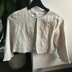 Beige linnebolero - Snygg beige bolero från mango i linne med rund halsringning och enkel knapp framtill. 152 men passar xs