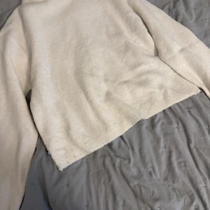 Ljusvit stickad tröja - Mysig ljusvit stickad tröja med lång ärm och rak passform. Tröjan har en enkel och clean look, perfekt att styla med jeans eller kjol. Ribbad kant nedtill och vid ärmslut för extra detalj. Superenkel att matcha och passar till lager-på-lager.