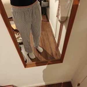 Randiga byxor från 157, storlek M - Säljer ett par sköna byxor från 157 i storlek M. De är vita med smala grå ränder, har resår i midjan och raka ben. Perfekta för en chill look och tillverkade i mjukt bomullstyg. Passar dig som gillar avslappnad stil. Korta i benen 