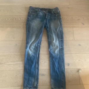 Jack & Jones Tim Slim Fit jeans blå - Snygga blå jeans från Jack & Jones, modell Tim Slim Fit. Jeansen har en klassisk femficksdesign, smal passform och slitna detaljer för en cool, avslappnad look. Tillverkade i mjukt denimtyg som sitter skönt hela dagen.