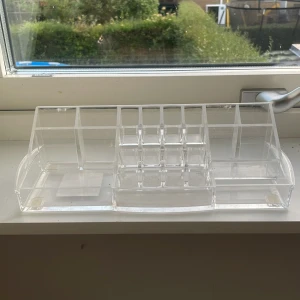Transparent sminkförvaring i akryl - Snygg och praktisk sminkförvaring i genomskinlig akryl med flera fack i olika storlekar. Perfekt för att organisera läppstift, borstar, ögonskuggor och andra sminkprodukter på sminkbordet eller i badrummet.