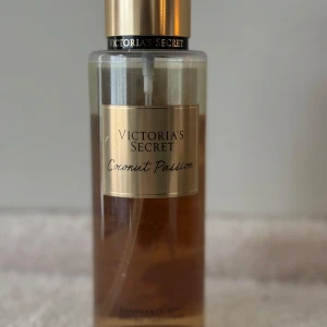 Victoria's Secret Coconut Passion mist - Fräsch body mist från Victoria's Secret i doften Coconut Passion. Flaskan är genomskinlig med guldigt lock och etikett, och innehållet har en ljusbrun nyans. Perfekt för dig som älskar tropiska och söta dofter med inslag av kokos.
