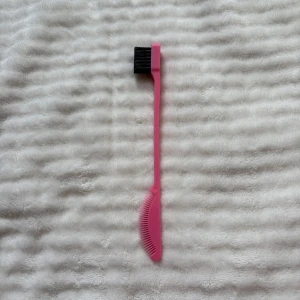 Rosa ögonbrynspenna/borste - Praktisk ögonbrynsborste i rosa plast med svart borst på ena sidan och en smal kam på andra sidan för att forma och separera bryn eller fransar. Perfekt för att få till snygga och definierade ögonbryn. Lätt att använda och ta med i sminkväskan.