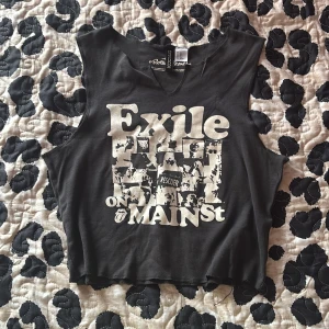 Rolling Stones croppad linnetopp - Svart croppad linnetopp med rå kant och tryck från Rolling Stones 'Exile on Main St'. Toppen är ärmlös och har en avslappnad passform, perfekt för dig som gillar bandmerch och rockig stil.