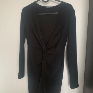 Svart omlottklänning från NLY One - Stilren svart kortklänning från NLY One med lång ärm och djup v-ringning. Klänningen har en snygg omlottdetalj framtill med twistad effekt i midjan. Perfekt för dig som gillar en enkel men elegant look.