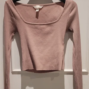 Ribbad rosa topp från H&M - Ribbad topp från H&M i en ljusrosa nyans. Modellen har lång ärm, fyrkantig ringning, kroppad och är figurnära med stretchigt material. 