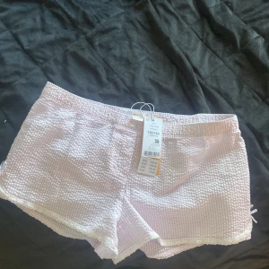 Rosa rutiga shorts med spetsdetalj - Söta ljusrosa shorts från Gina Tricot Young i rutigt tyg med mjuk struktur. De har elastisk midja, små knappar framtill och spetskant längs benen. En liten rosett i sidan ger extra gullig touch. Perfekta för varma sommardagar!Prislappen e kvar!!